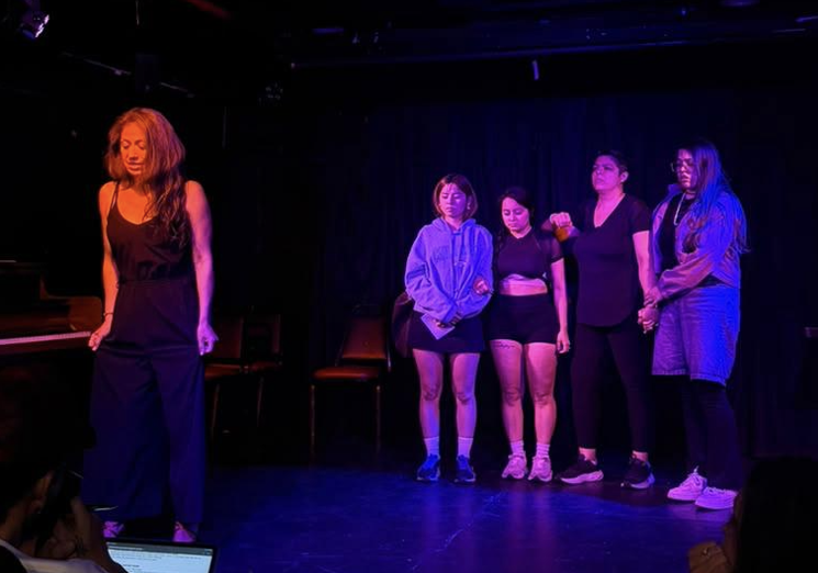 Actress singing on stage with an ensemble of women behind her