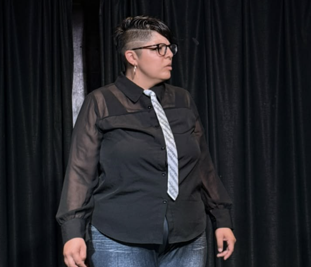 Actress in a sheer black shirt and tie standing on stage