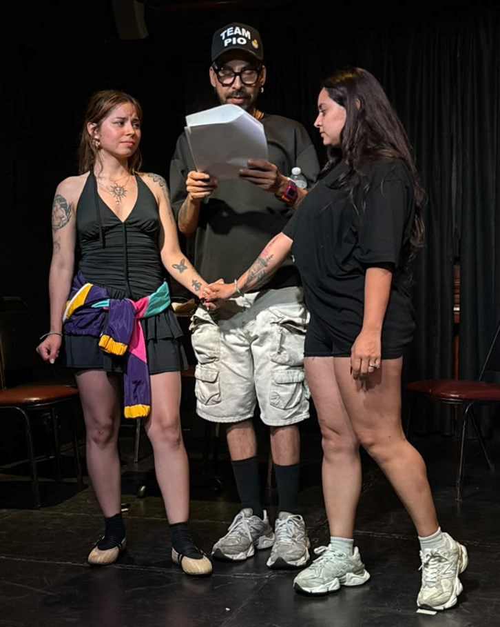 Three cast members in a scene, one reading from a script